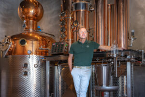 Anbefalet alt-tekst: Henrik Nerst fra Wild Distillery står foran det specialbyggede kobber-destilleringsapparat fra Müller Brennereianlagen til produktion af bornholmsk gin.